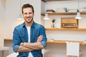 Portrait of smiling young businessman with armcrossed at office